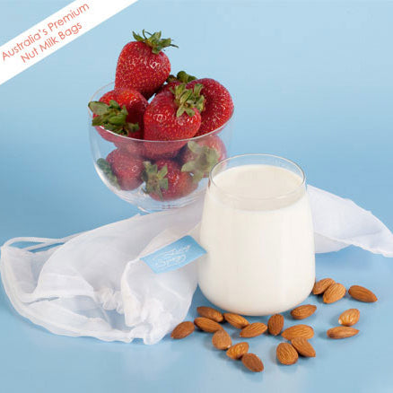 Living Synergy nut milk bag with glass of nut milk and bowl of strawberries.